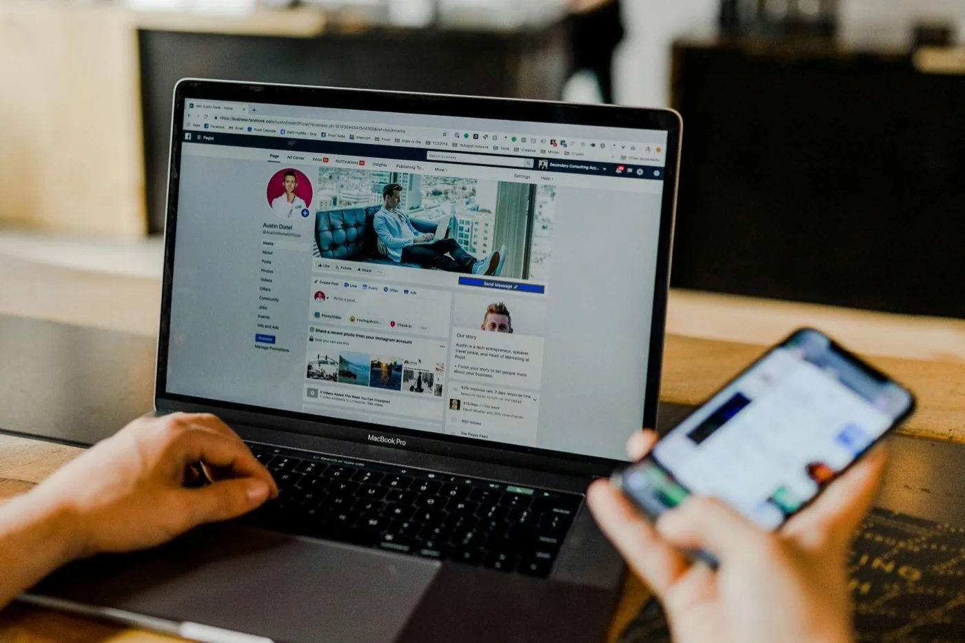 A person browsing a Facebook business page on a laptop while holding a phone