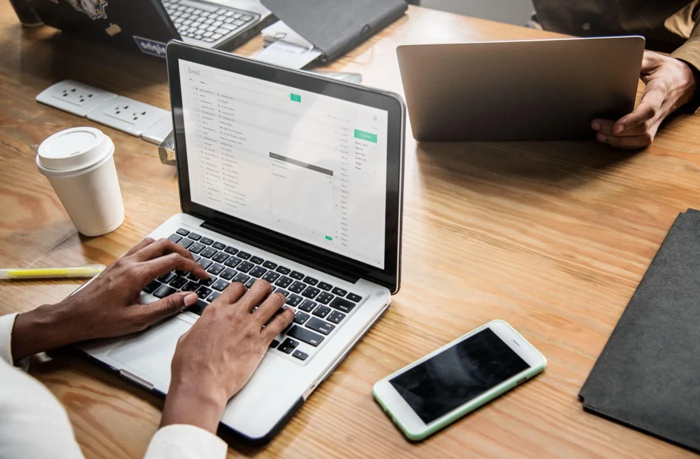 Hands typing an email on a laptop at a shared desk