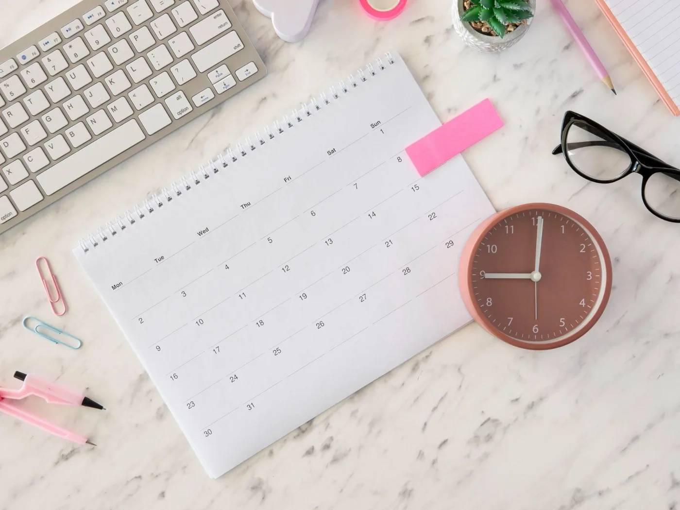 A desk flat-lay with a blank calendar, a clock, and stationery