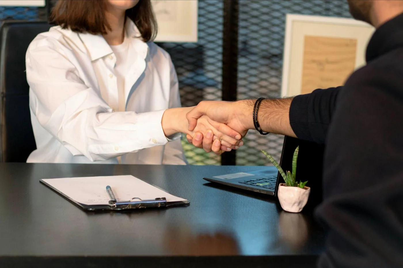 A consultant and a new client shaking hands across a desk after signing an agreement