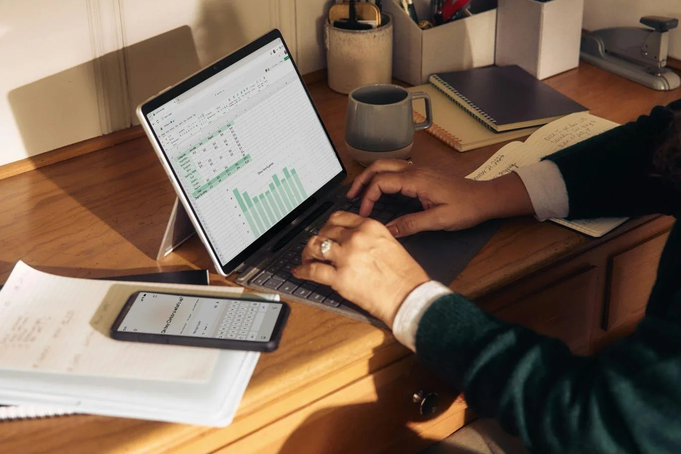 A person working through a spreadsheet with a bar chart on a laptop at a sunlit home desk