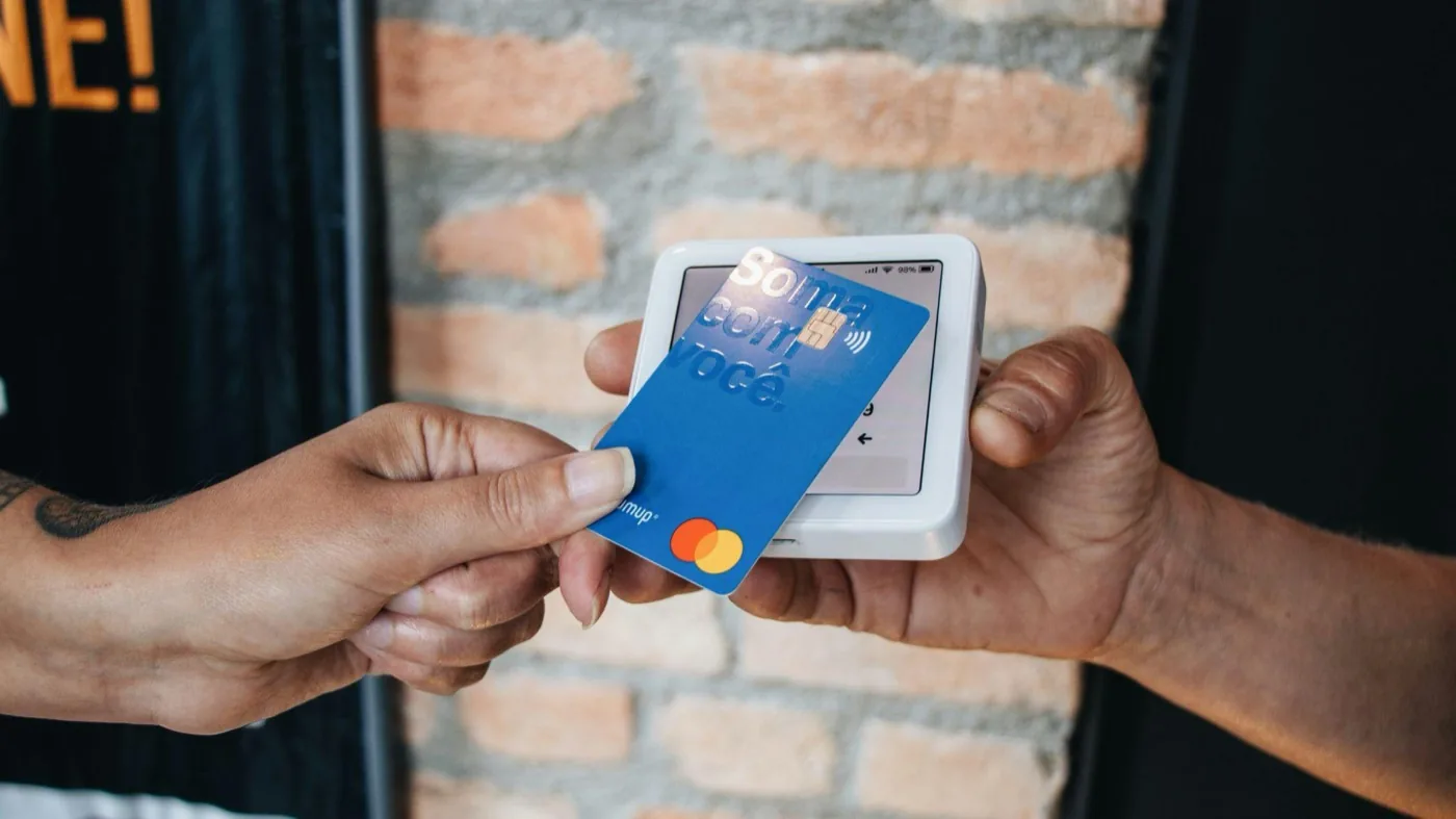 A customer tapping a bank card on a contactless payment terminal held by a vendor