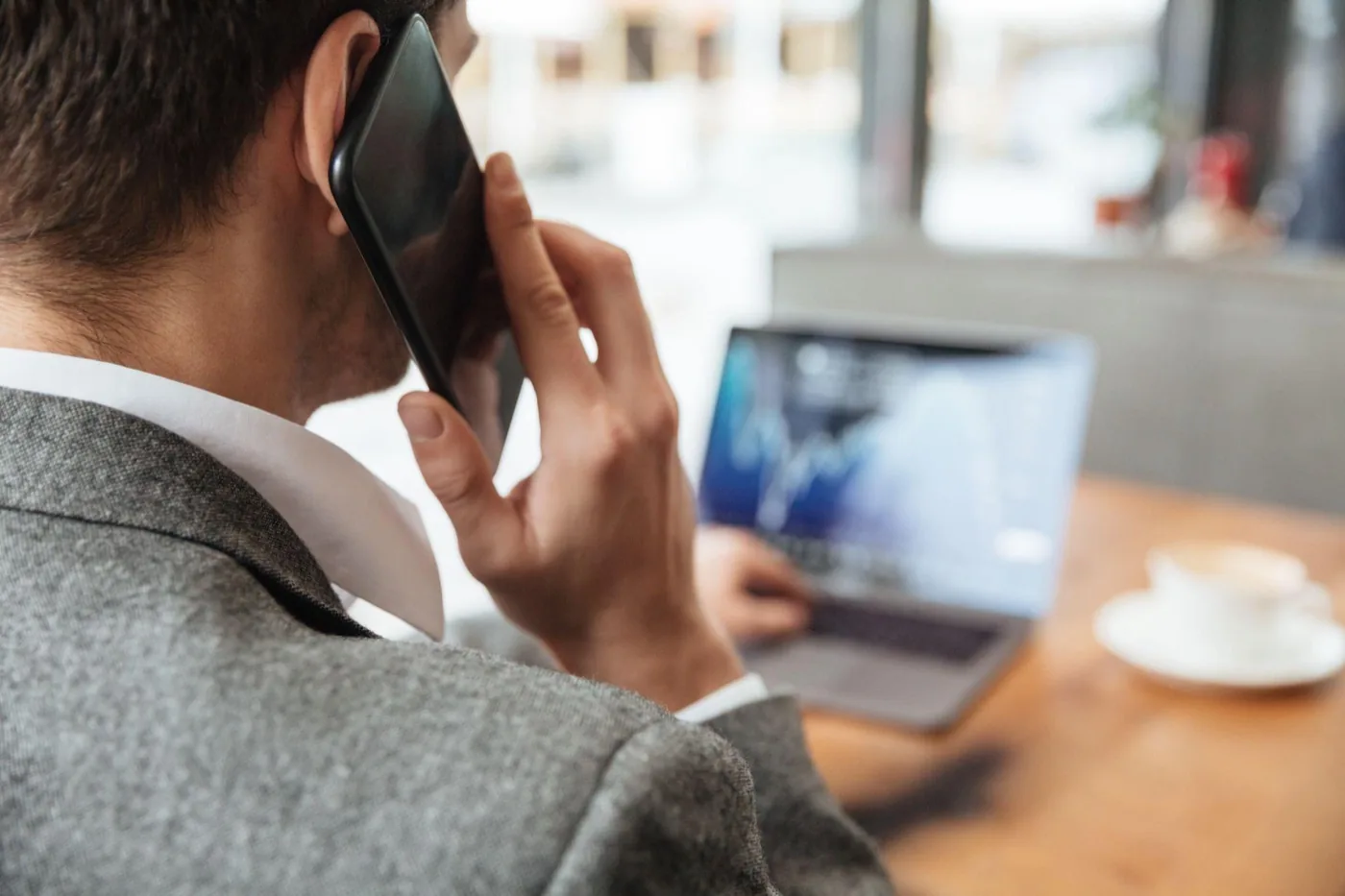 A man in a suit taking a phone call while looking at a chart on his laptop