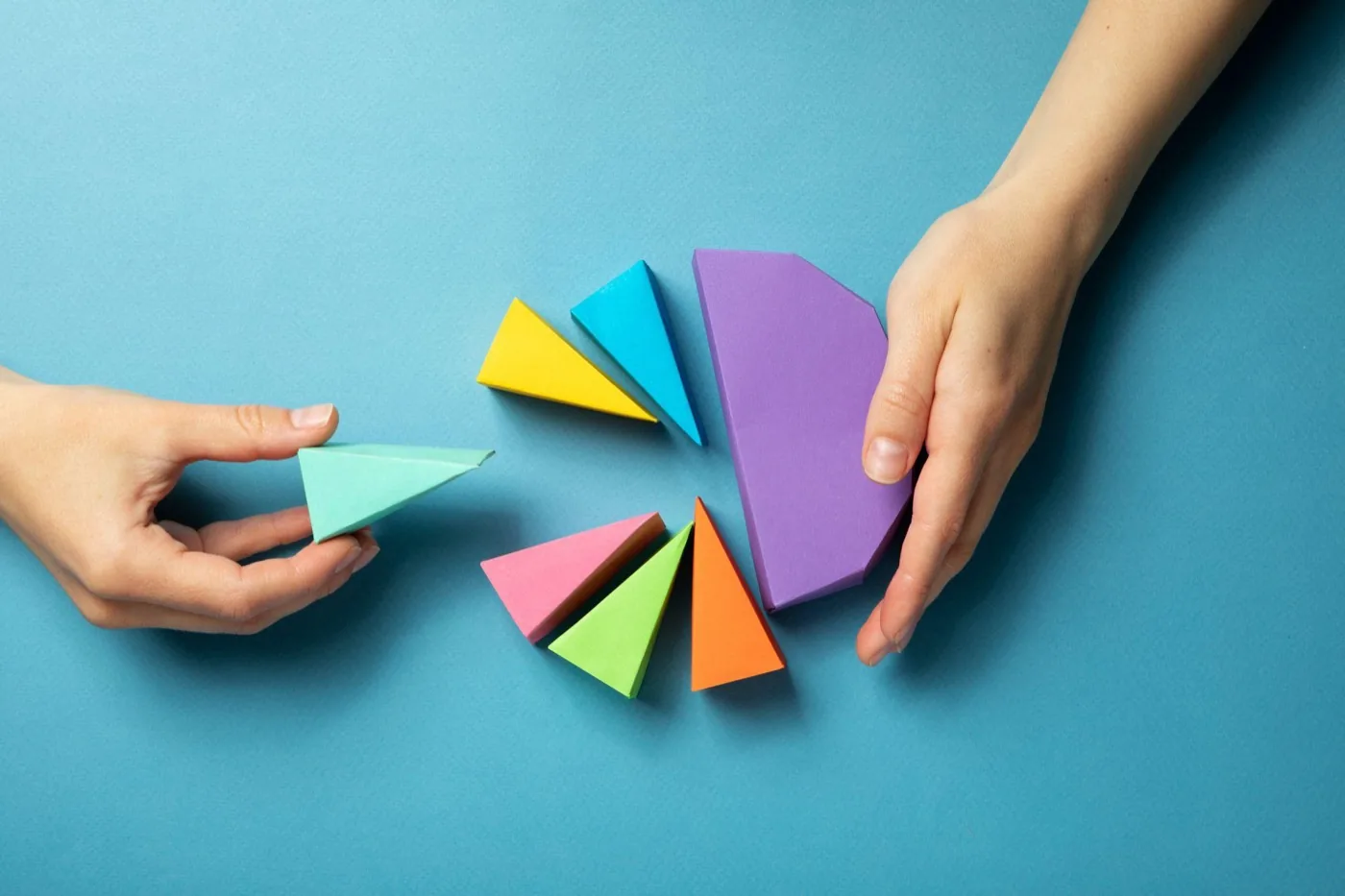 Two hands sorting colourful paper triangles into groups on a blue background